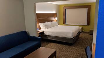 A hotel room with a bed, a blue sofa, a wooden coffee table, and a nightstand with a lamp.