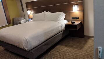 A hotel room with a large bed, bedside tables, a lamp, and a control panel.