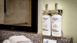 Dove body lotion and hand wash bottles on a bathroom counter with a towel stack and a sign indicating extra amenities. - Holiday Inn Express & Suites Claypool Hill (Richlands Area) by IHG (Pounding Mill)