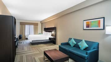 A hotel room with a bed, a sofa, a coffee table, a desk with a chair, and a painting on the wall.