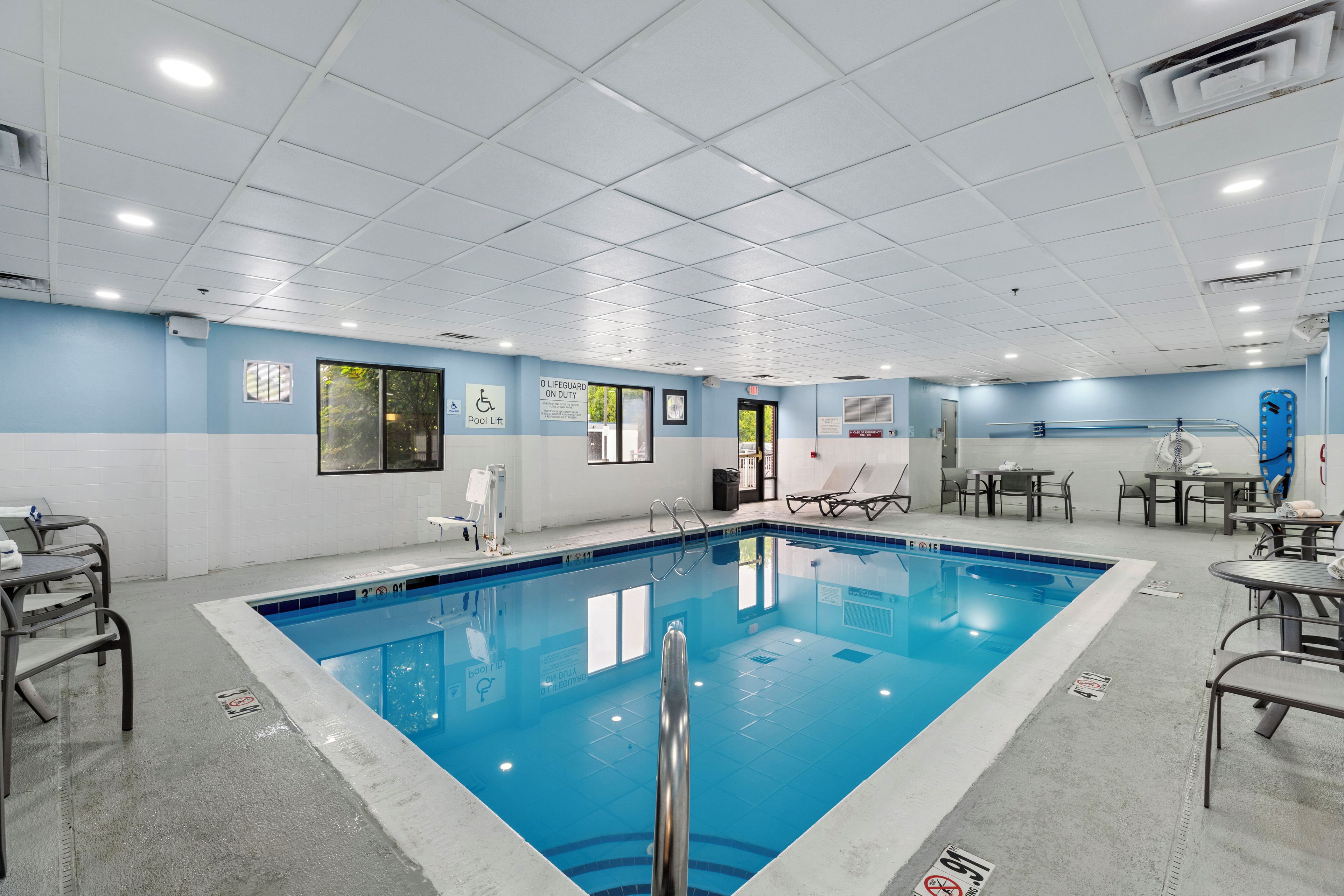 A swimming pool area with a lifeguard on duty sign, pool lift, and lounge chairs.