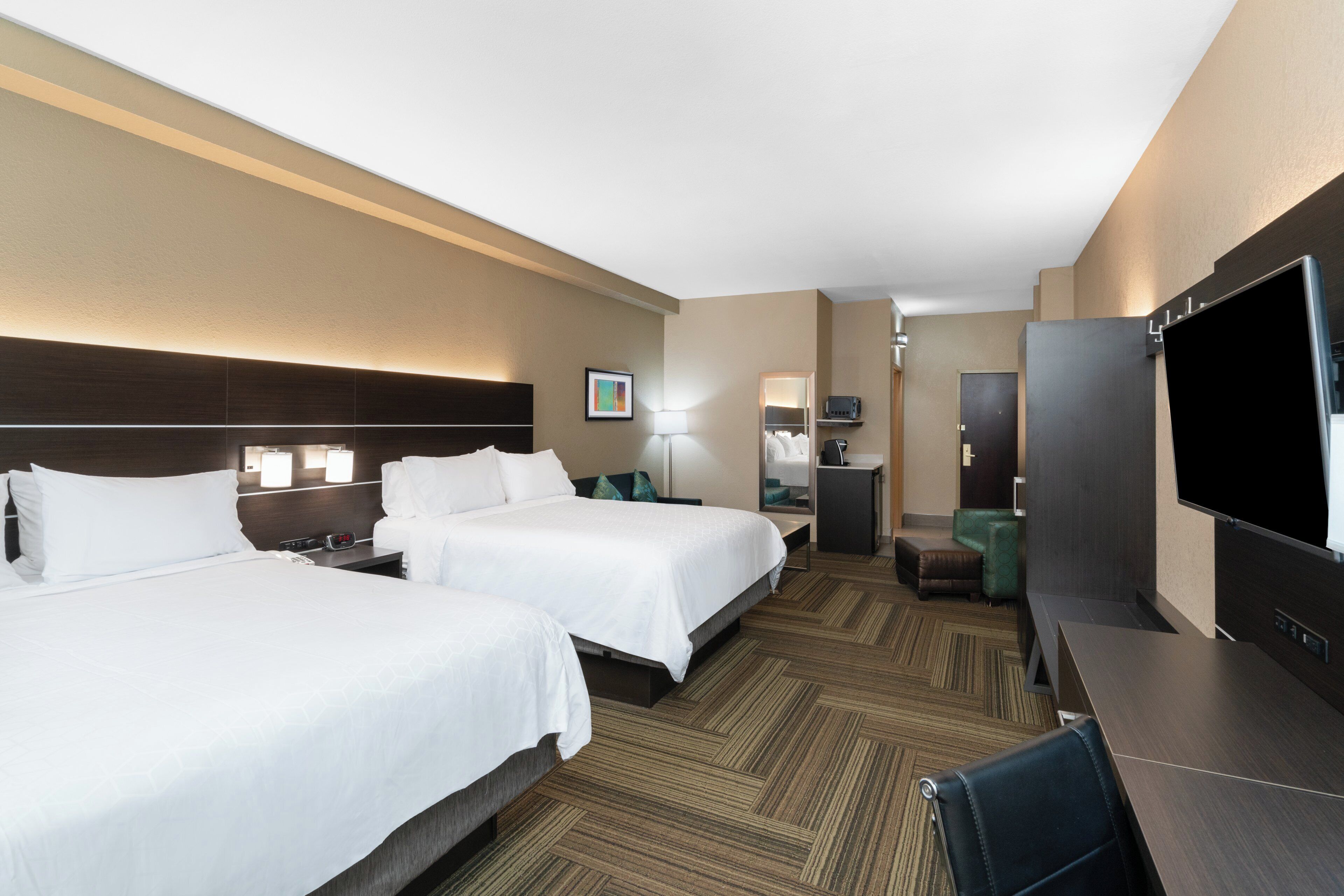 A hotel room with two beds, a desk, a television, and a mirror.