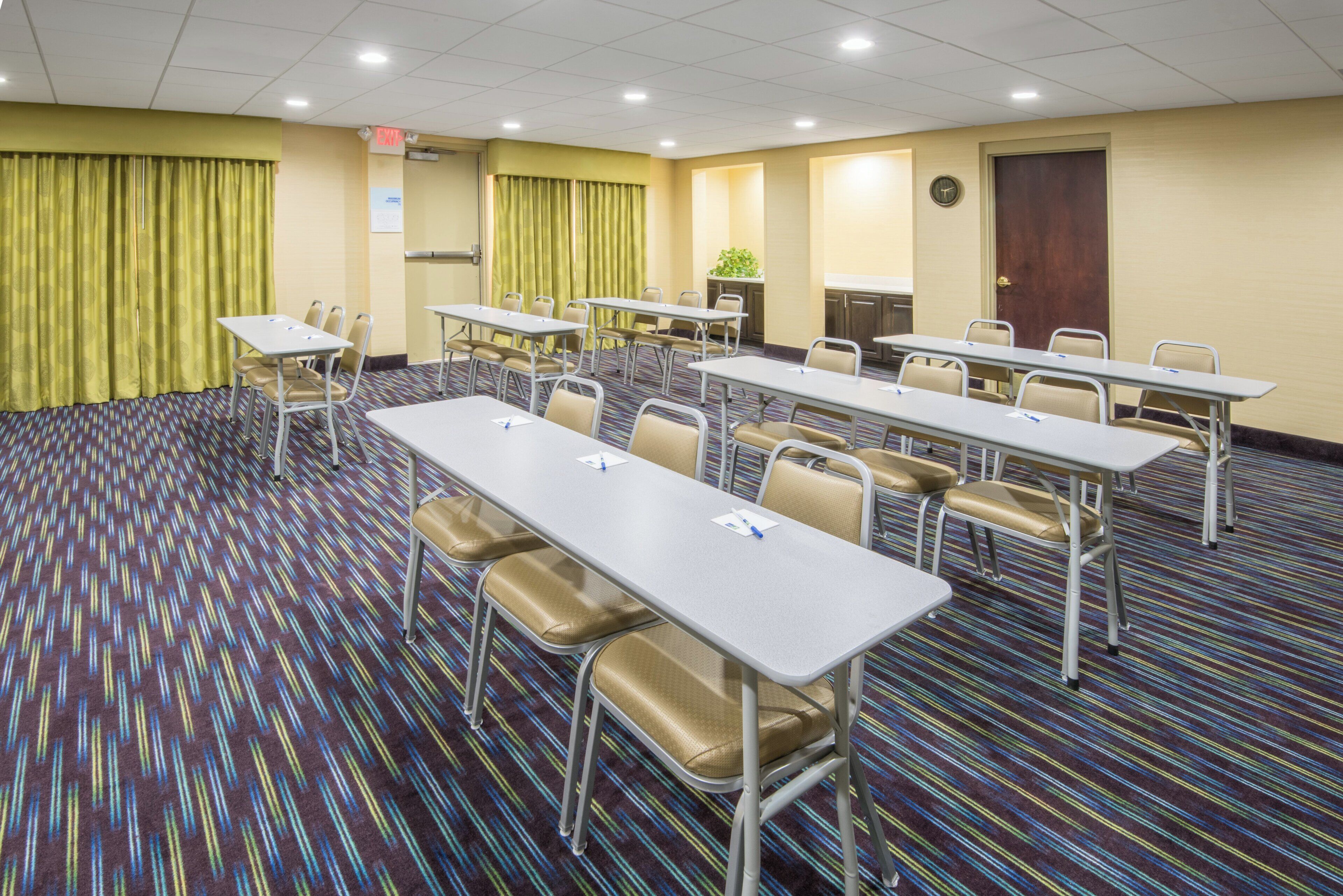 A conference room with multiple tables and chairs, a clock on the wall, and an exit sign.