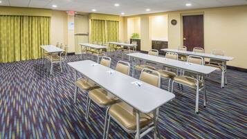A conference room with multiple tables and chairs, a clock on the wall, and an exit sign.