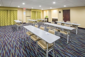 A conference room with multiple tables and chairs, a clock on the wall, and an exit sign.