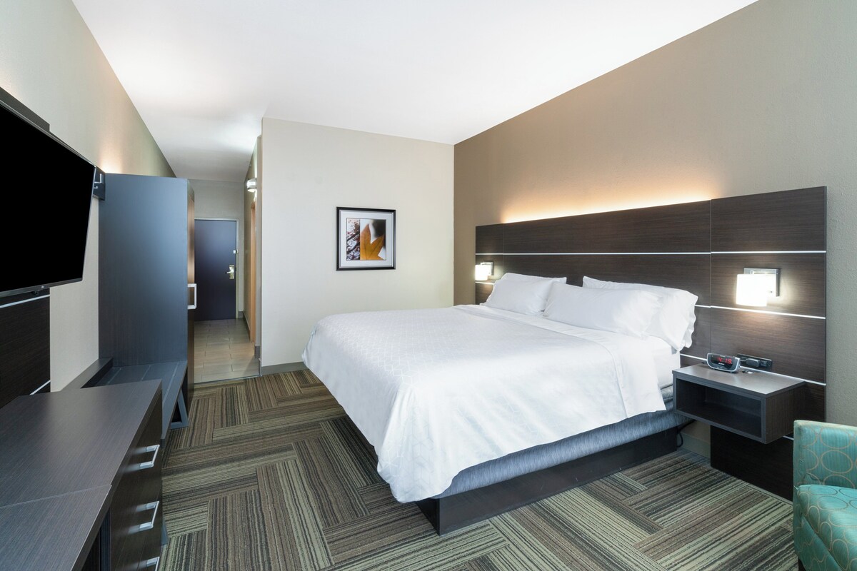 A hotel room with a bed, bedside table, TV, and a framed picture on the wall.