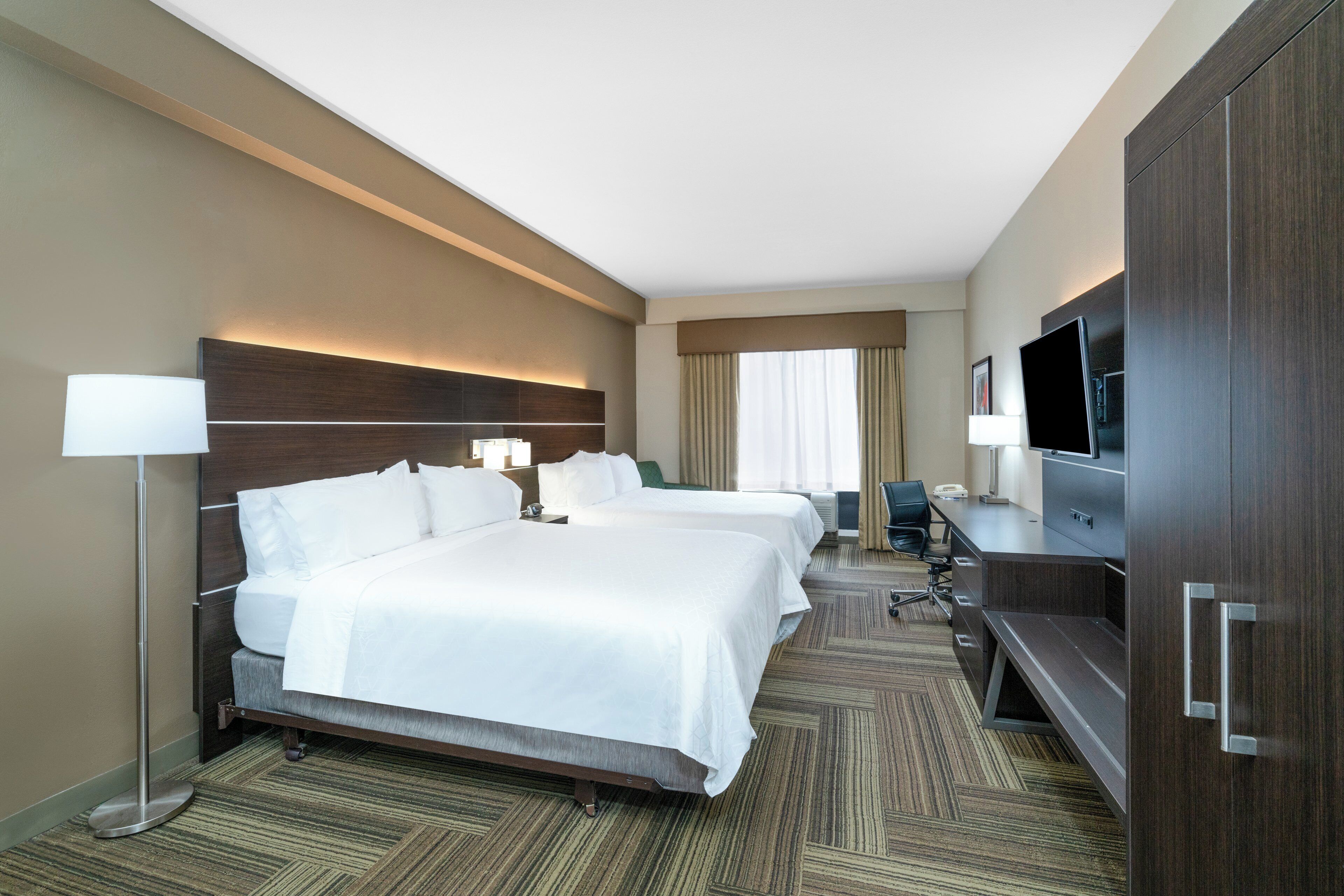 Habitación de hotel con dos camas, un escritorio, un televisor y un armario grande.