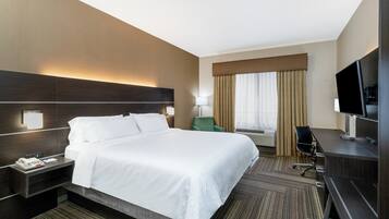 Habitación de hotel con una cama grande, un escritorio con televisor, una silla, una lámpara y una ventana con cortinas.