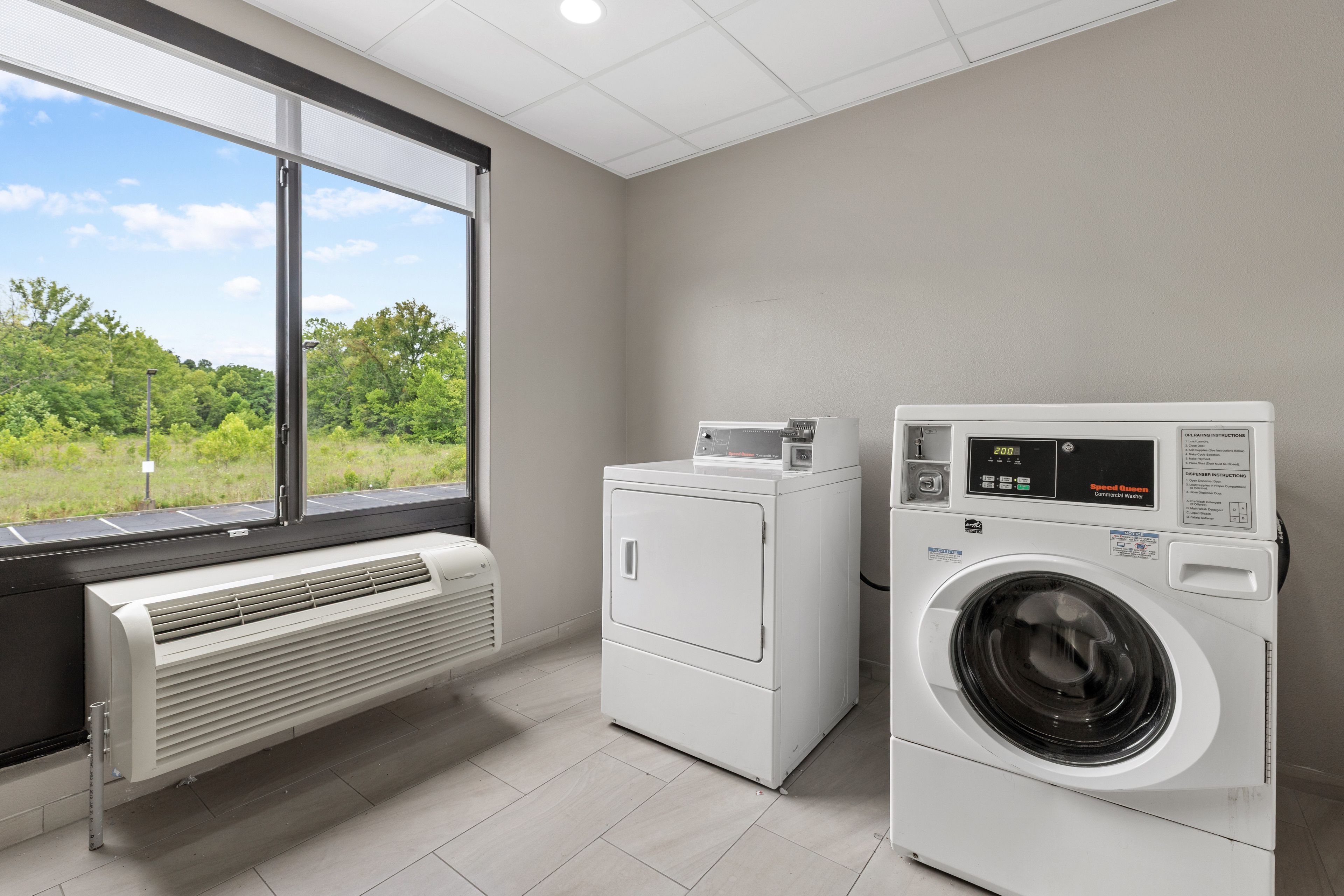 A laundry room with a large window, a wall-mounted heater, and a front-loading washing machine.