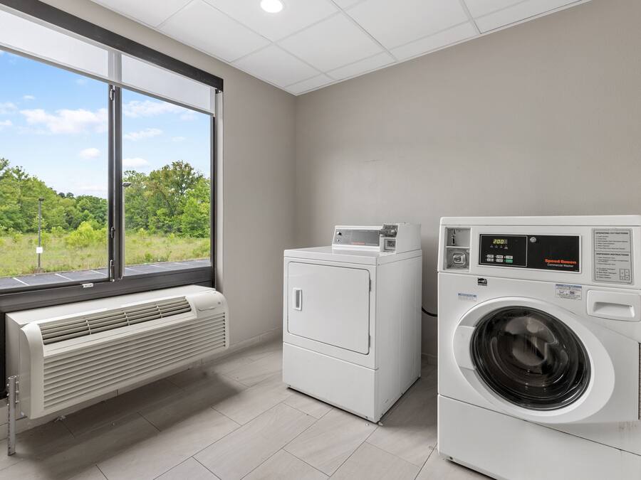 A laundry room with a large window, a wall-mounted heater, and a front-loading washing machine.