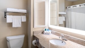 A bathroom with a toilet, sink, and mirror. There are towels on a rack and a shower curtain.
