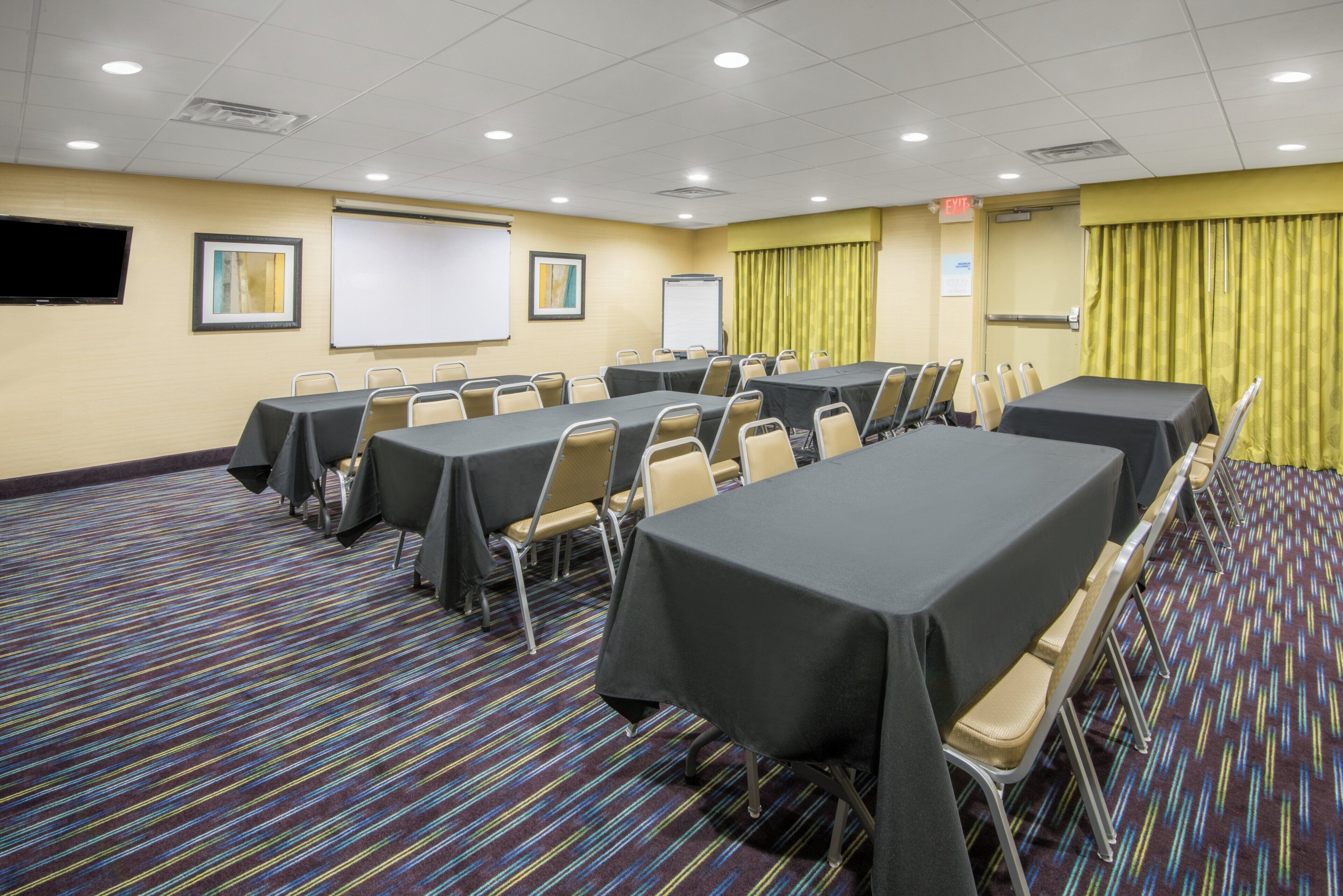 Un salón de conferencias con mesas, sillas, una pantalla de proyector y una pizarra.