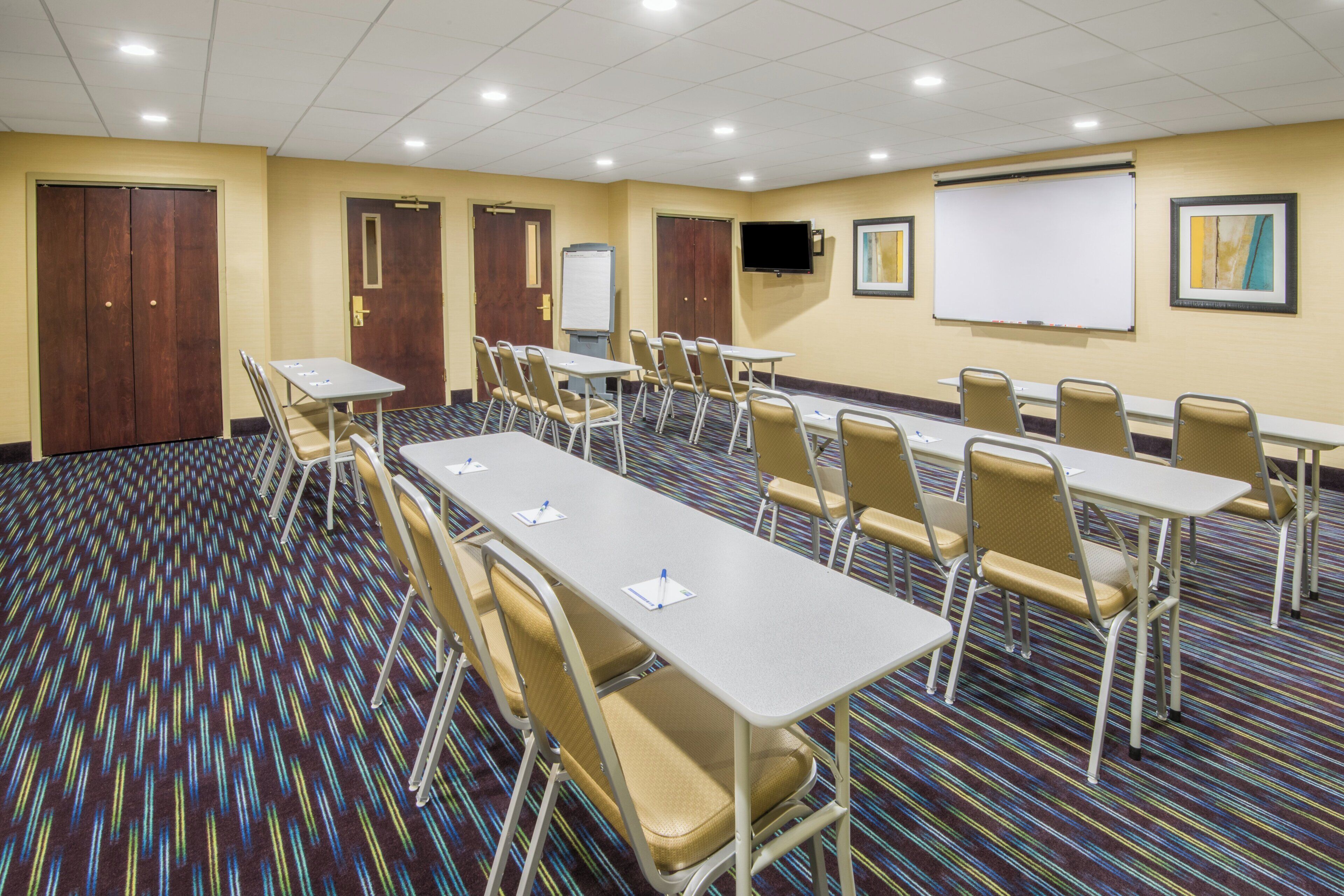 A conference room with multiple tables and chairs, a whiteboard, and a projector screen.