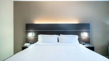 A hotel room with a large bed, two bedside tables, a nightstand, and a wall-mounted lamp.