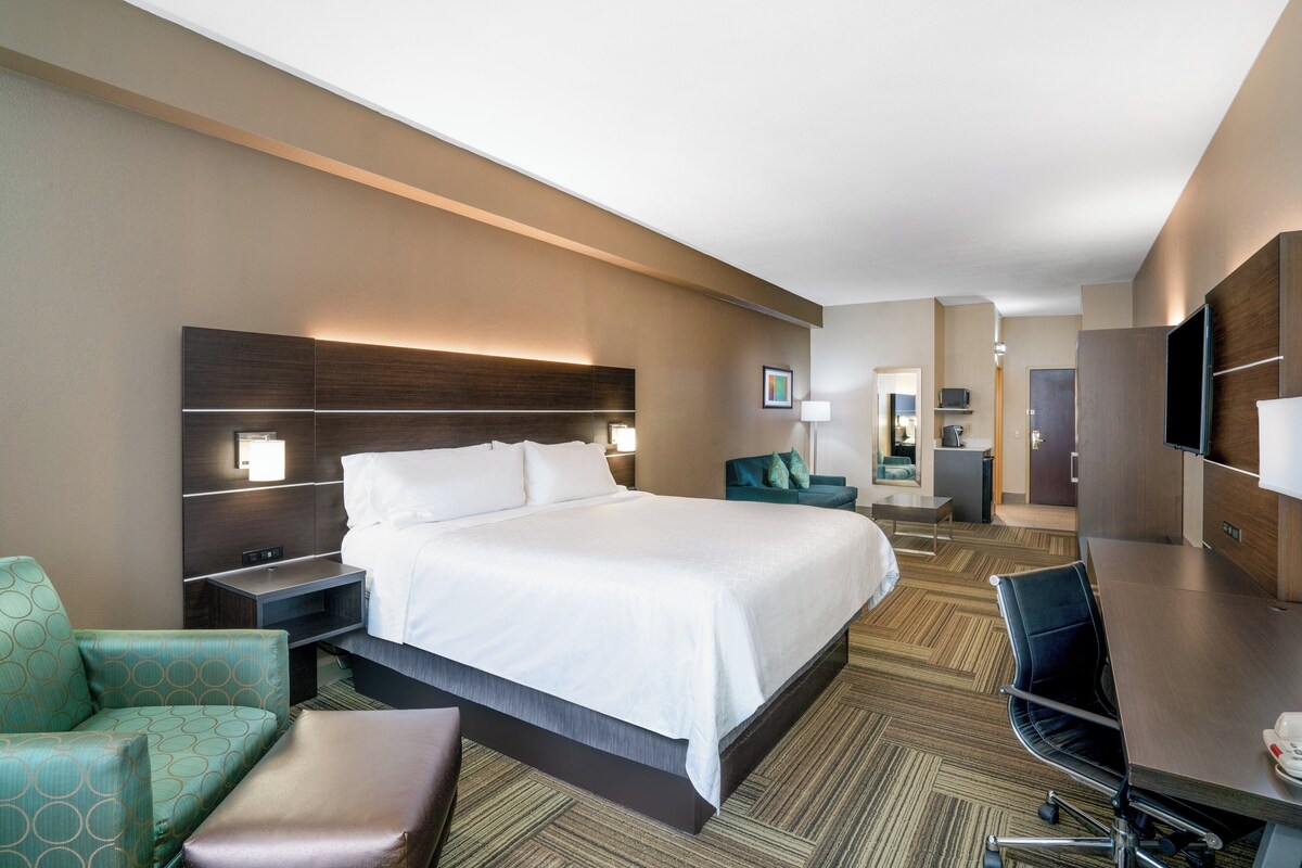 A hotel room with a bed, a desk, a chair, a sofa, and a TV.