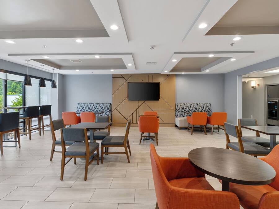 Un espace repas moderne avec des tables et des chaises, un téléviseur à écran plat fixé au mur et un réfrigérateur.