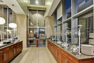 A modern kitchen with wooden cabinets, stainless steel appliances, and a buffet setup with glassware and plates.