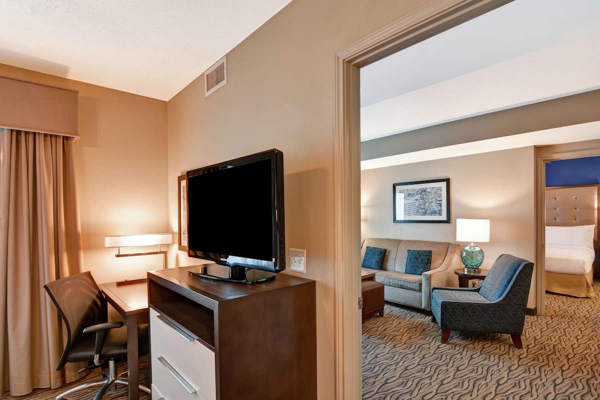 A hotel room with a desk, chair, television, sofa, and armchair.