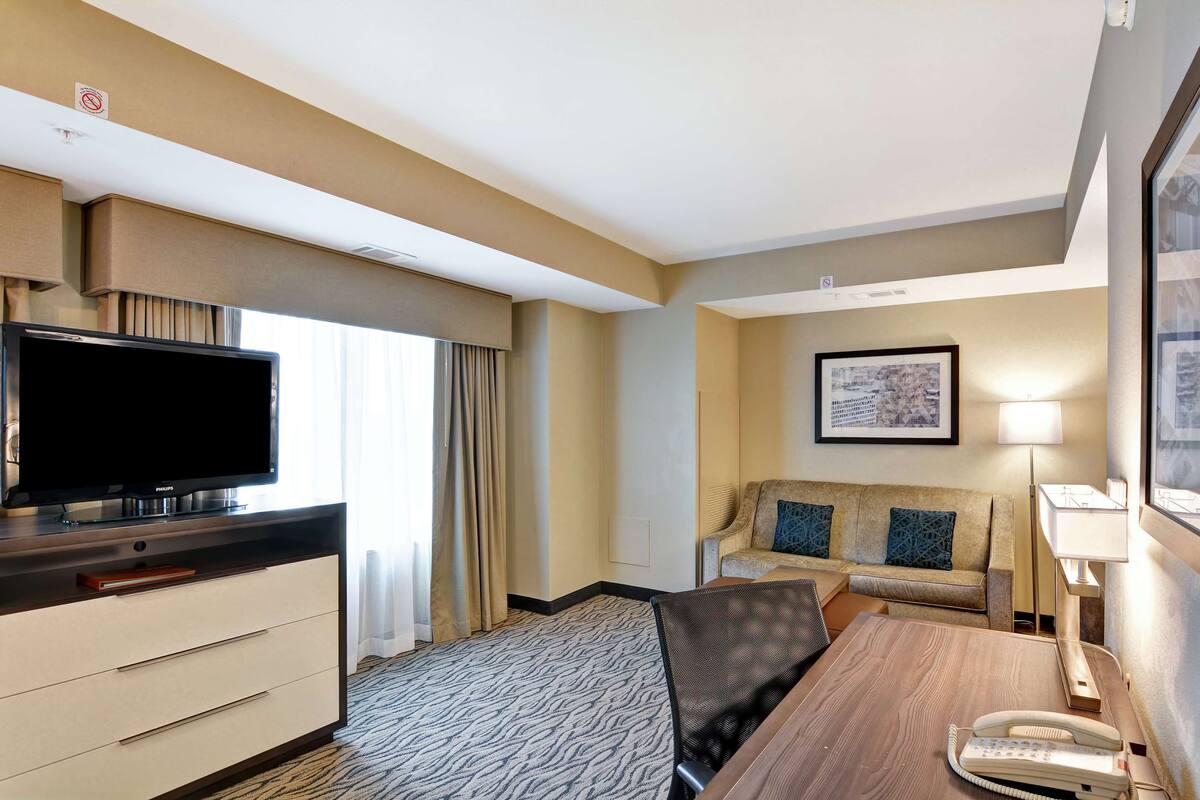 A hotel room with a flat-screen TV, a sofa, a desk with a telephone, and a framed picture on the wall.