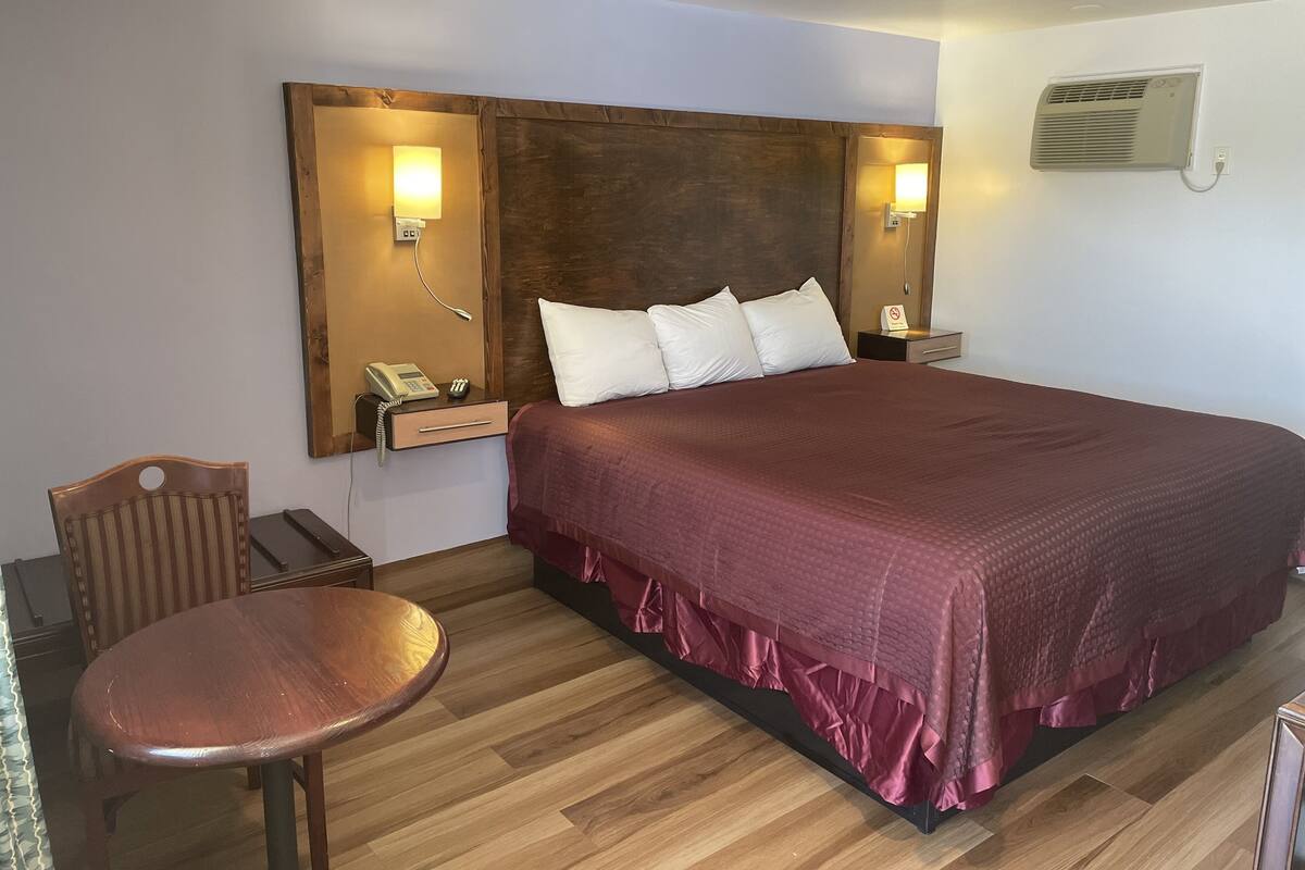 A hotel room with a large bed, a wooden headboard, bedside lamps, a telephone, a nightstand, a chair, and a wooden floor.