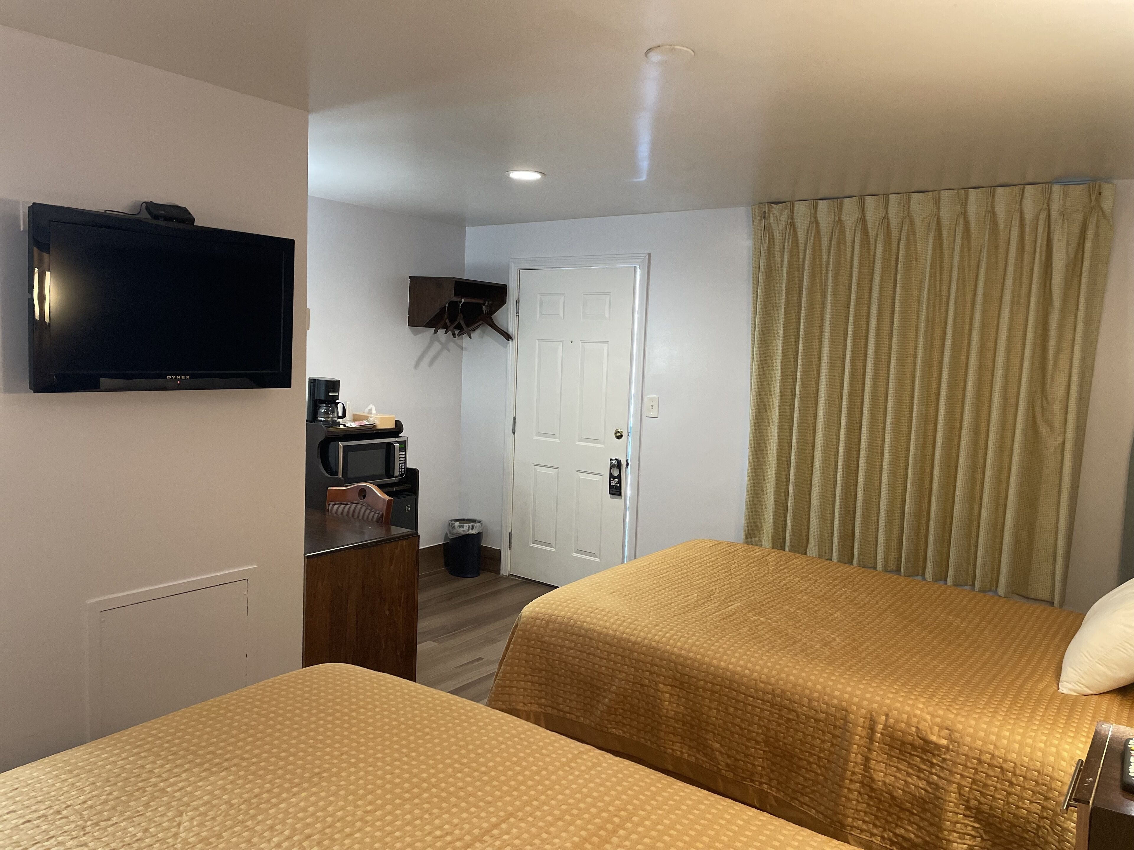 A hotel room with two beds, a TV, a desk with a microwave, and a door with a coat rack.