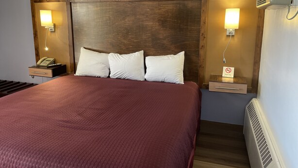 A hotel room with a large bed, wooden headboard, bedside lamps, a telephone, and a sign indicating no smoking.