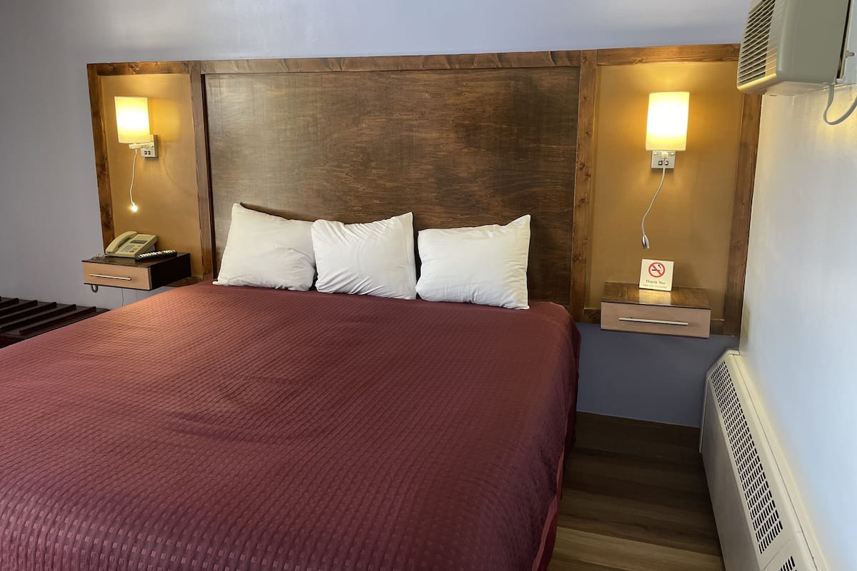 A hotel room with a large bed, wooden headboard, bedside lamps, a telephone, and a sign indicating no smoking.