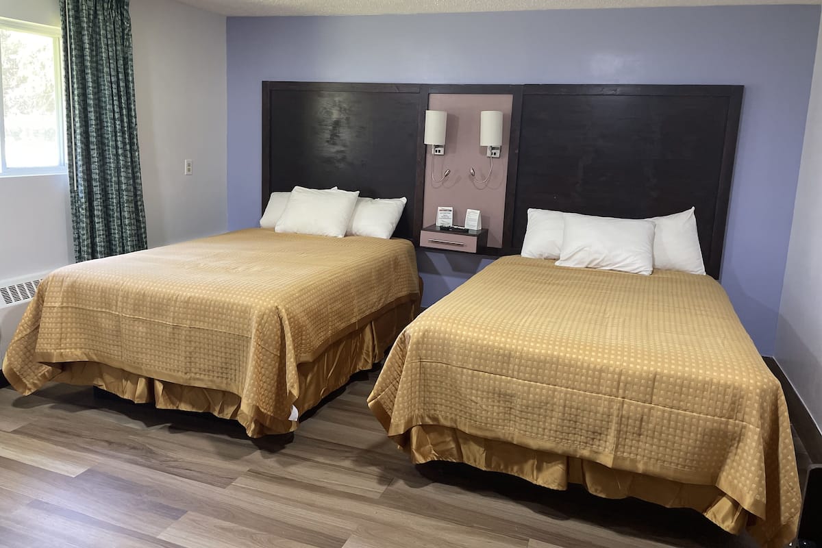 Two double beds with beige bedding, a dark headboard, a wall-mounted phone, and a window with curtains.