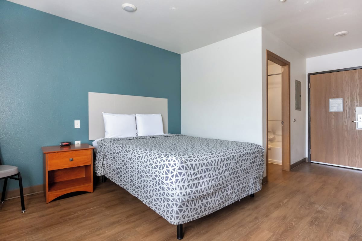 A bedroom with a bed, a nightstand, a chair, and a wooden door.