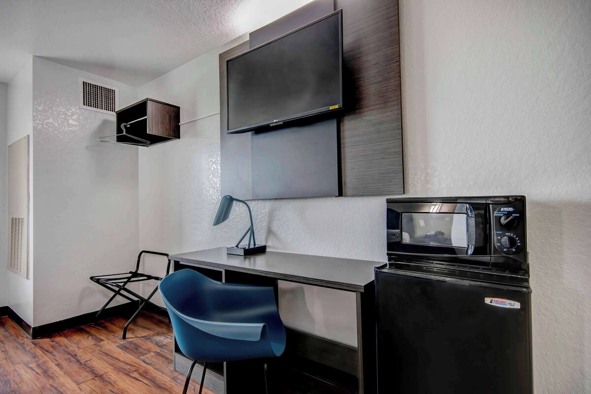 Una kitchenette compacta con microondas, un refrigerador pequeño, un televisor sobre la encimera y una silla azul.