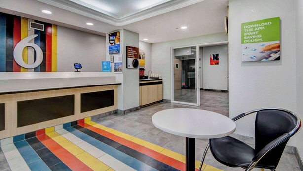 Eine moderne Hotelhalle mit einer Rezeption, einem farbenfrohen Streifen Teppich, einem runden Tisch mit einem Stuhl und einem an der Wand befestigten Schild, das eine App bewirbt.