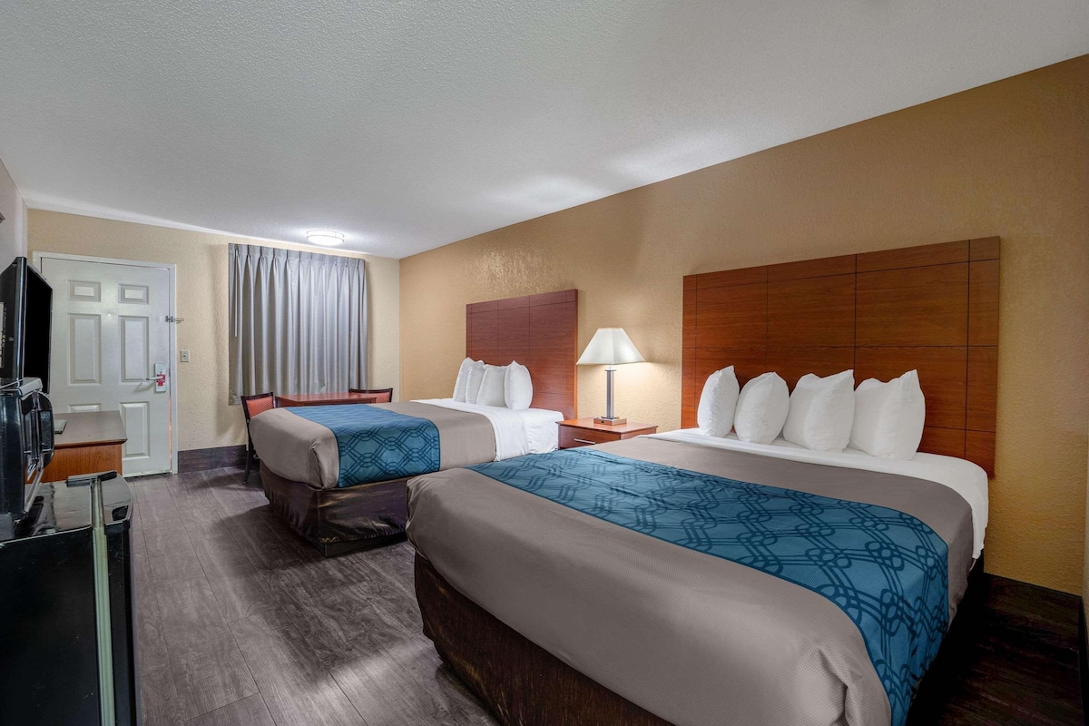 A hotel room with two beds, a desk with a chair, a TV, and a window with curtains.