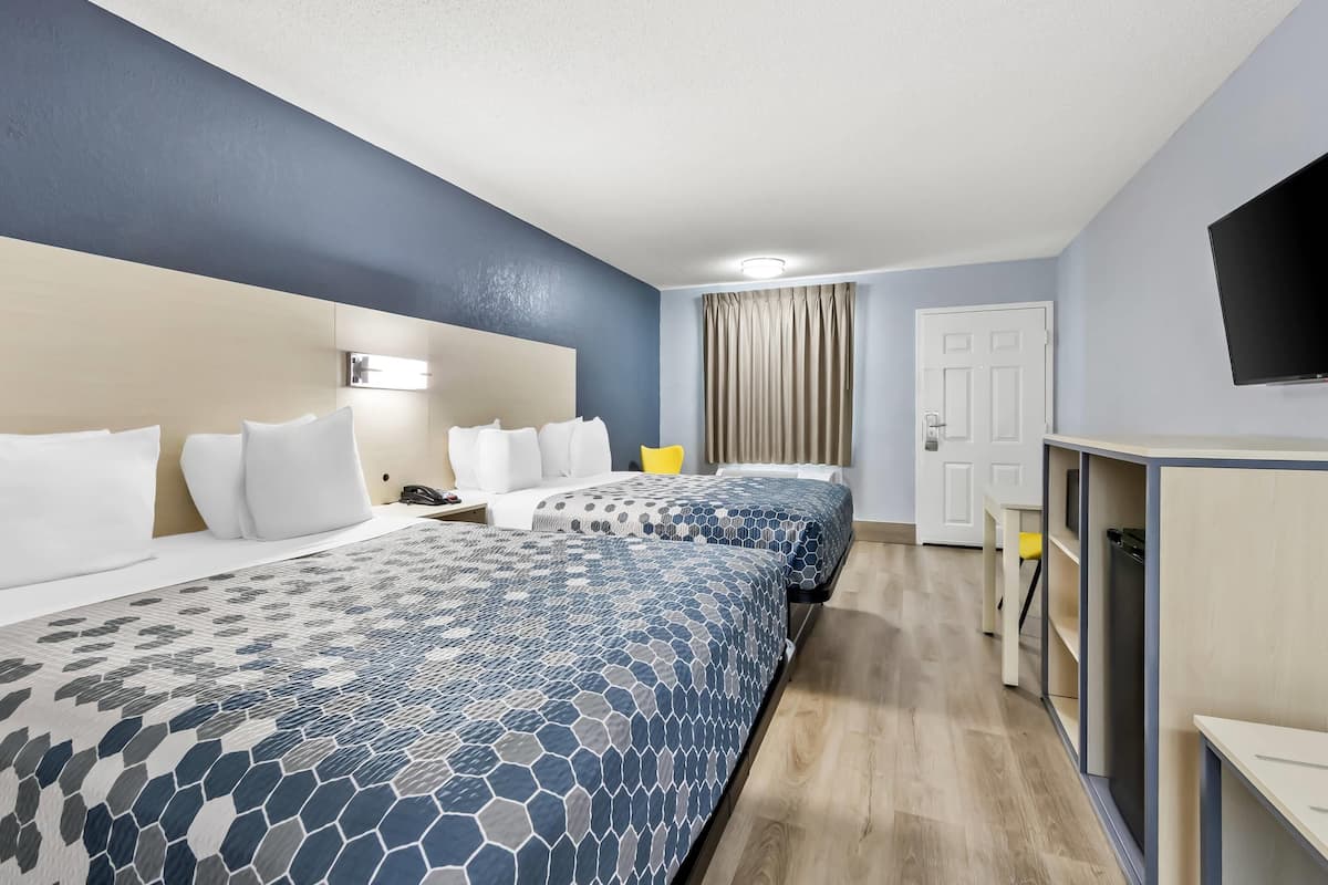 A hotel room with two beds, a desk, a television, and a door.