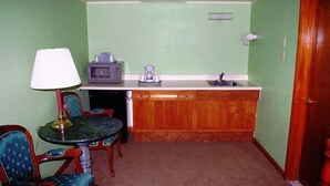 Una habitación compacta con kitchenette, una mesa de comedor con sillas, una lámpara y una cama con colcha colorida.