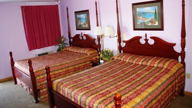 Un dormitorio con dos camas de madera, un ventilador de techo, cortinas rojas y dos cuadros en la pared.