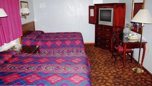 Una habitación de hotel con una cama grande, un escritorio con silla, un televisor y un espejo.
