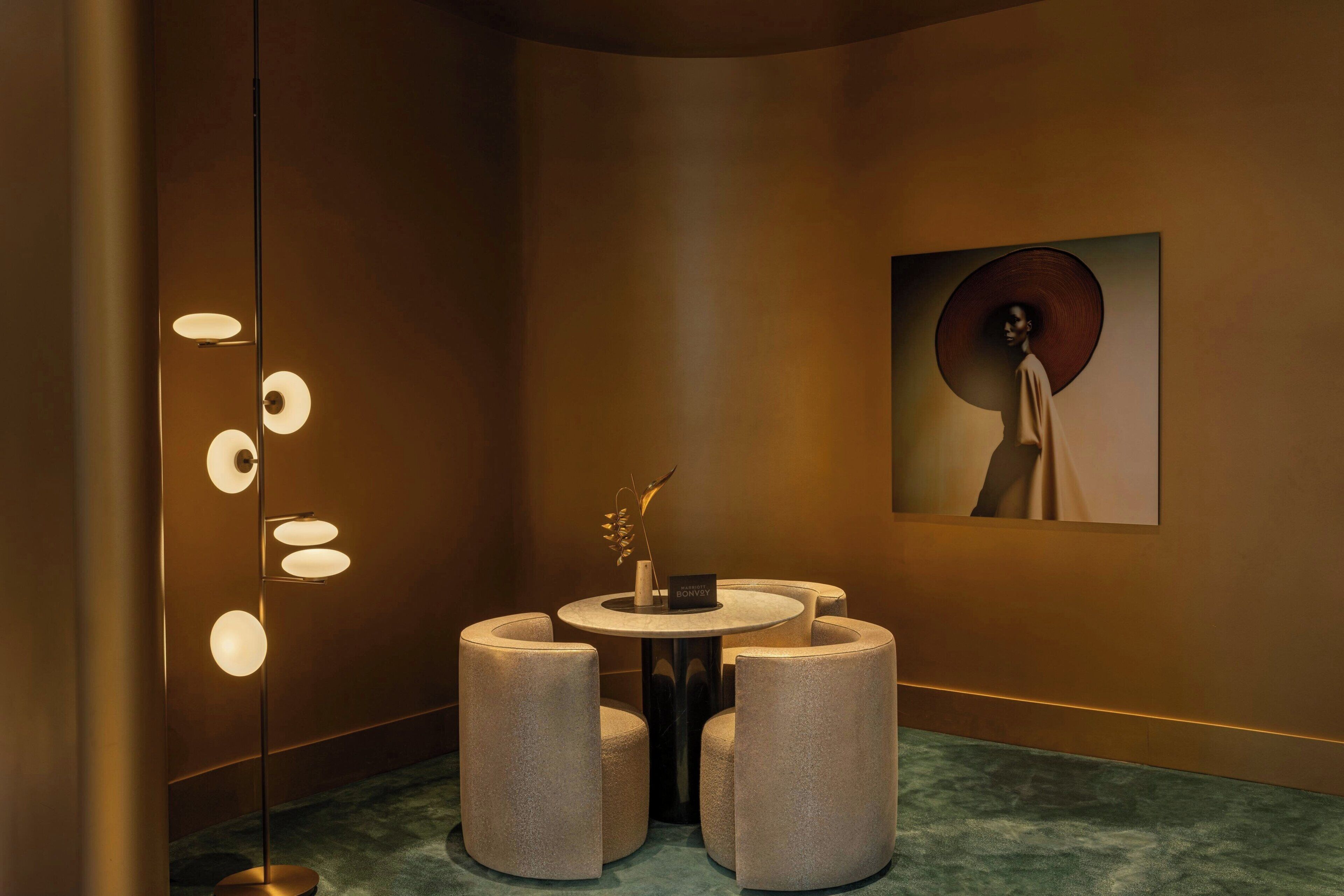 A modern interior with a round table, four cylindrical stools, a floor lamp, and a framed artwork on the wall.
