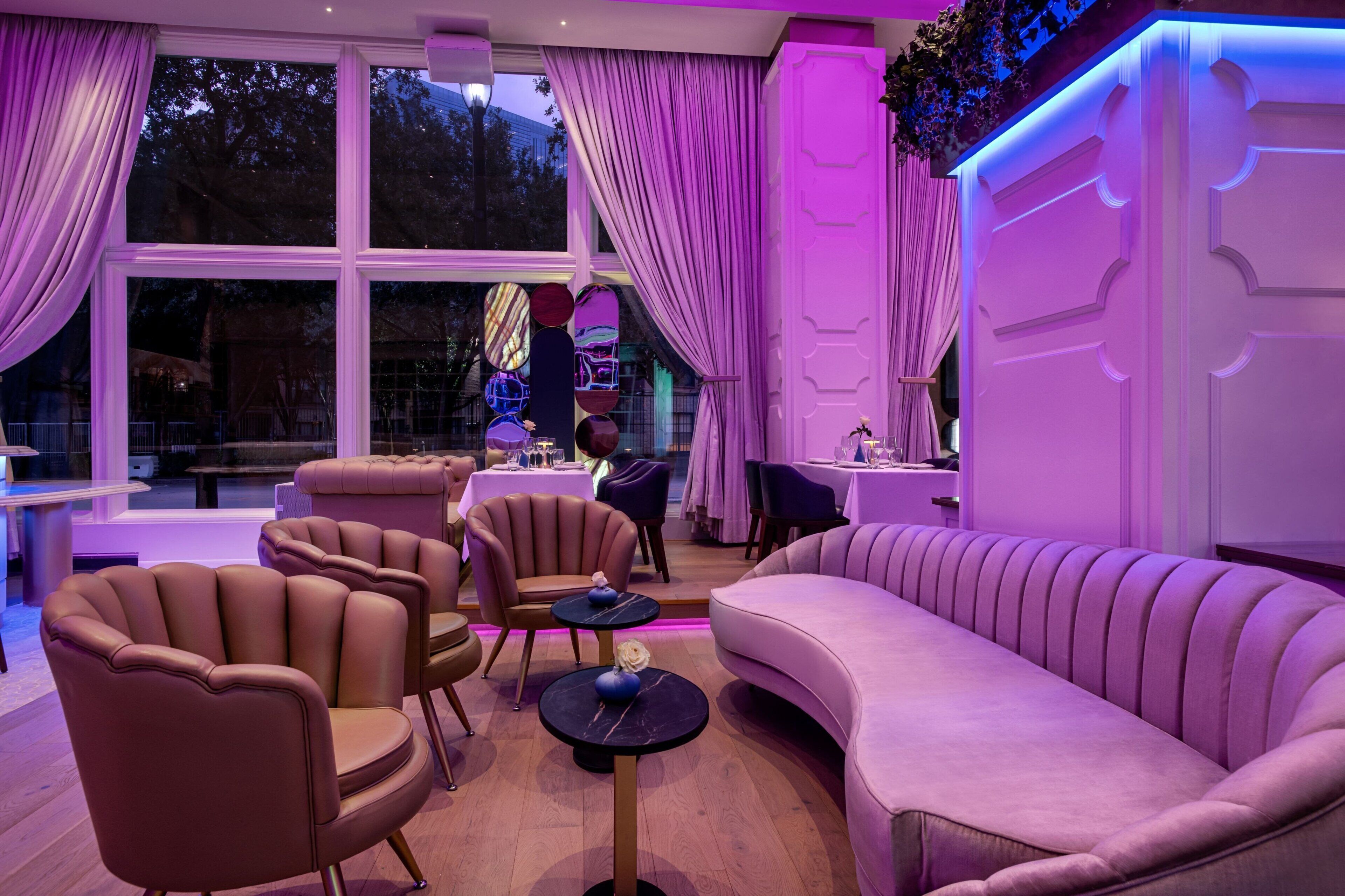 A modern interior with leather armchairs, a pink sofa, and a dining area with tables and chairs.