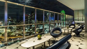 Um bar no terraço com vista panorâmica da cidade, mobiliário moderno e guarda-corpo de vidro.