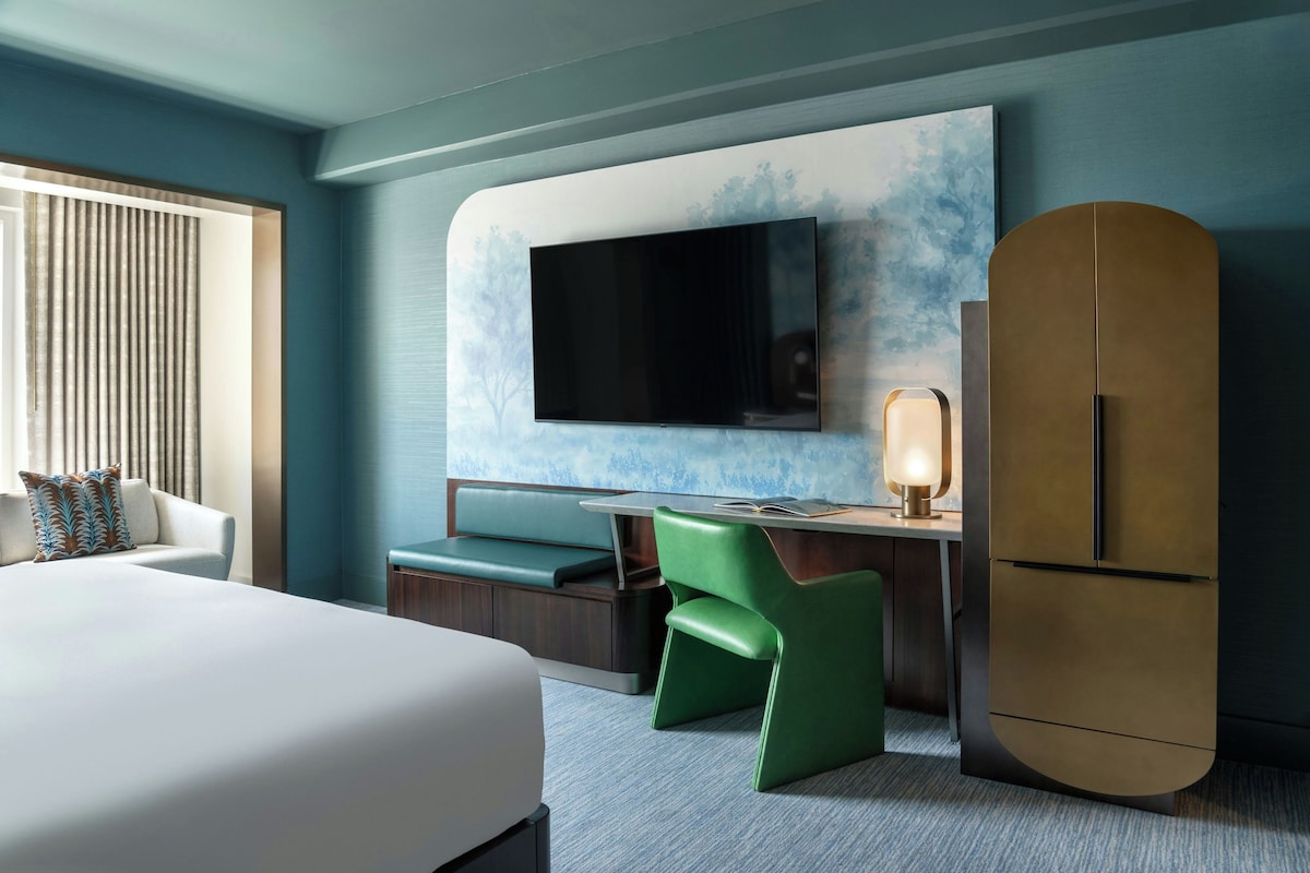 Una camera d'albergo con un letto, una scrivania con una sedia, una televisione e un frigorifero.