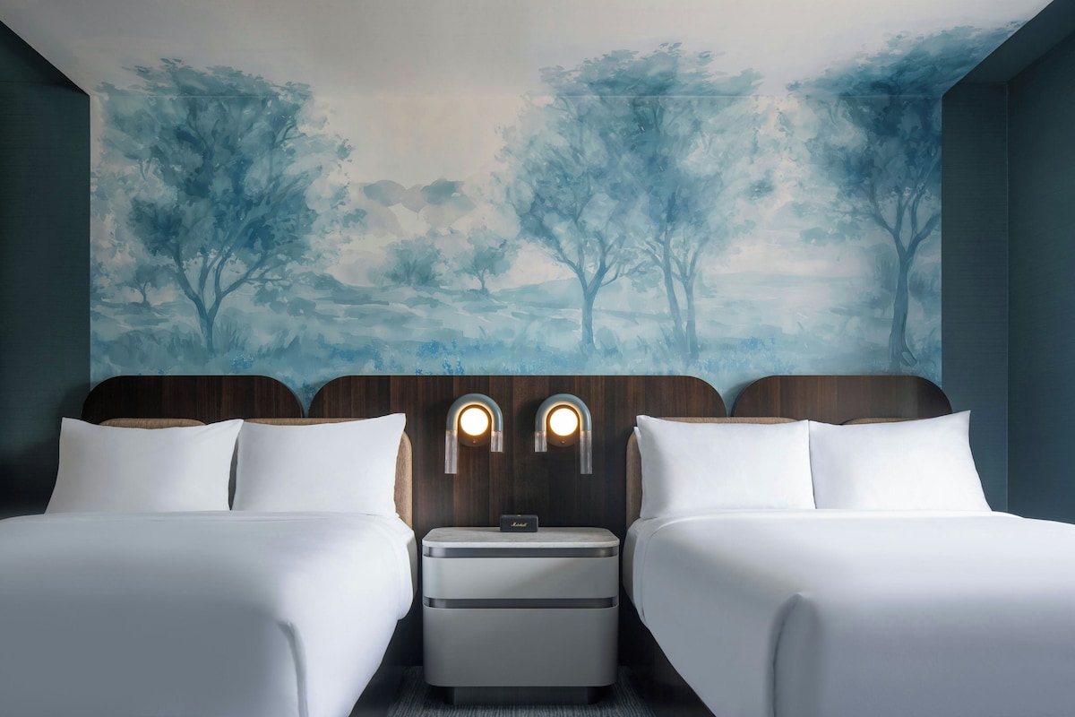 Una camera d'albergo con due letti, un comodino e un affresco sulla parete.