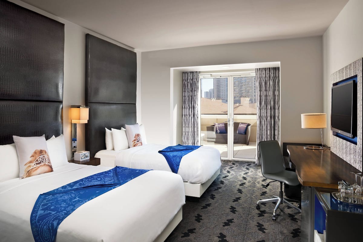 Ein Hotelzimmer mit zwei Betten, einem Schreibtisch, einem Fernseher und Blick auf die Stadt durch das Fenster.