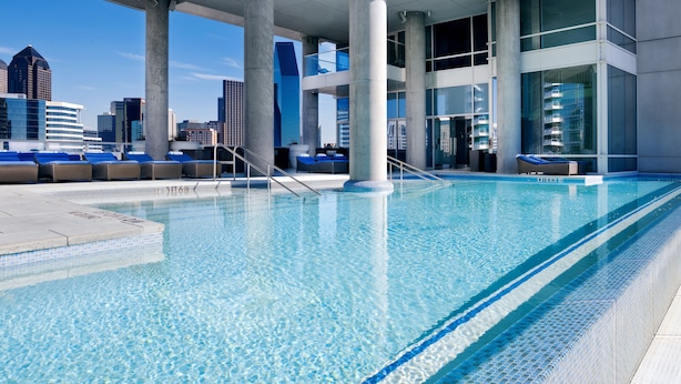 Piscina no terraço com água azul cristalina, rodeada por espreguiçadeiras e pilares de concreto.
