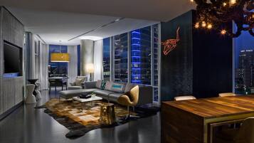 A modern living room with a large TV, a sofa, a dining table, and a view of the city at night.