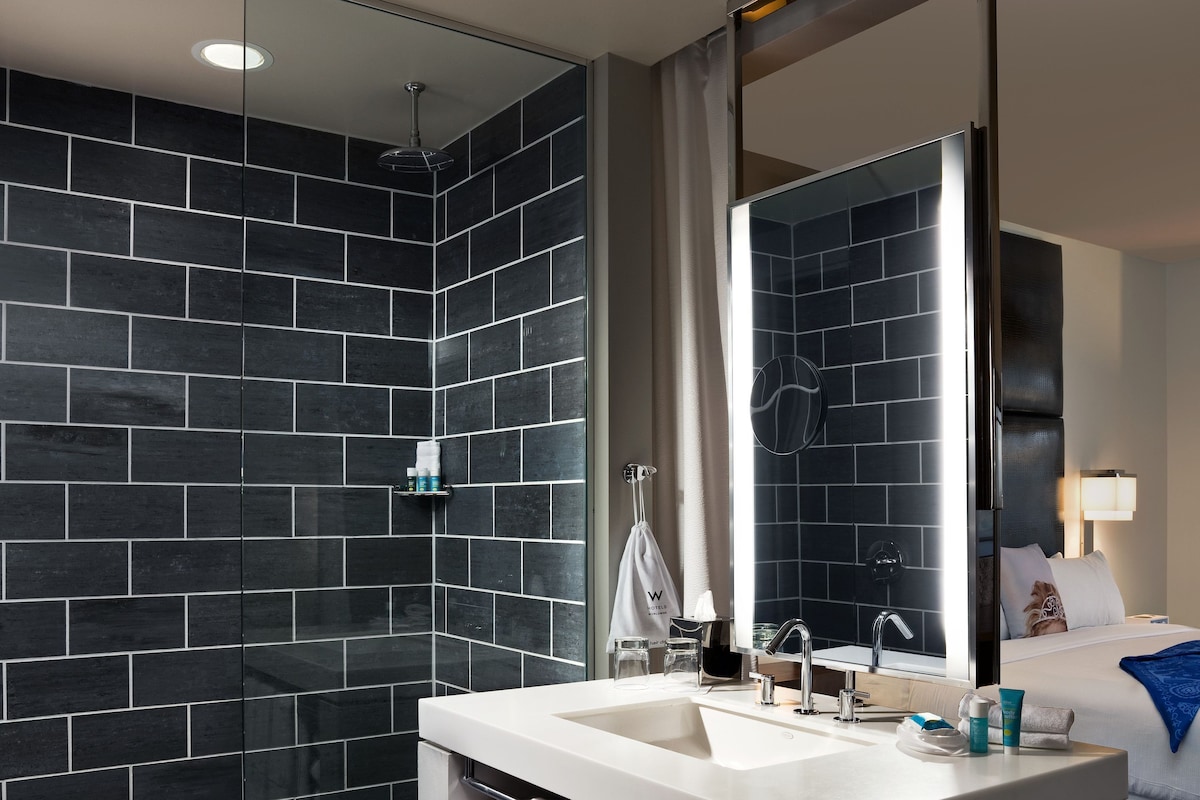 Un bagno moderno con uno specchio grande, due lavabi e una cabina doccia rivestita di piastrelle nere.