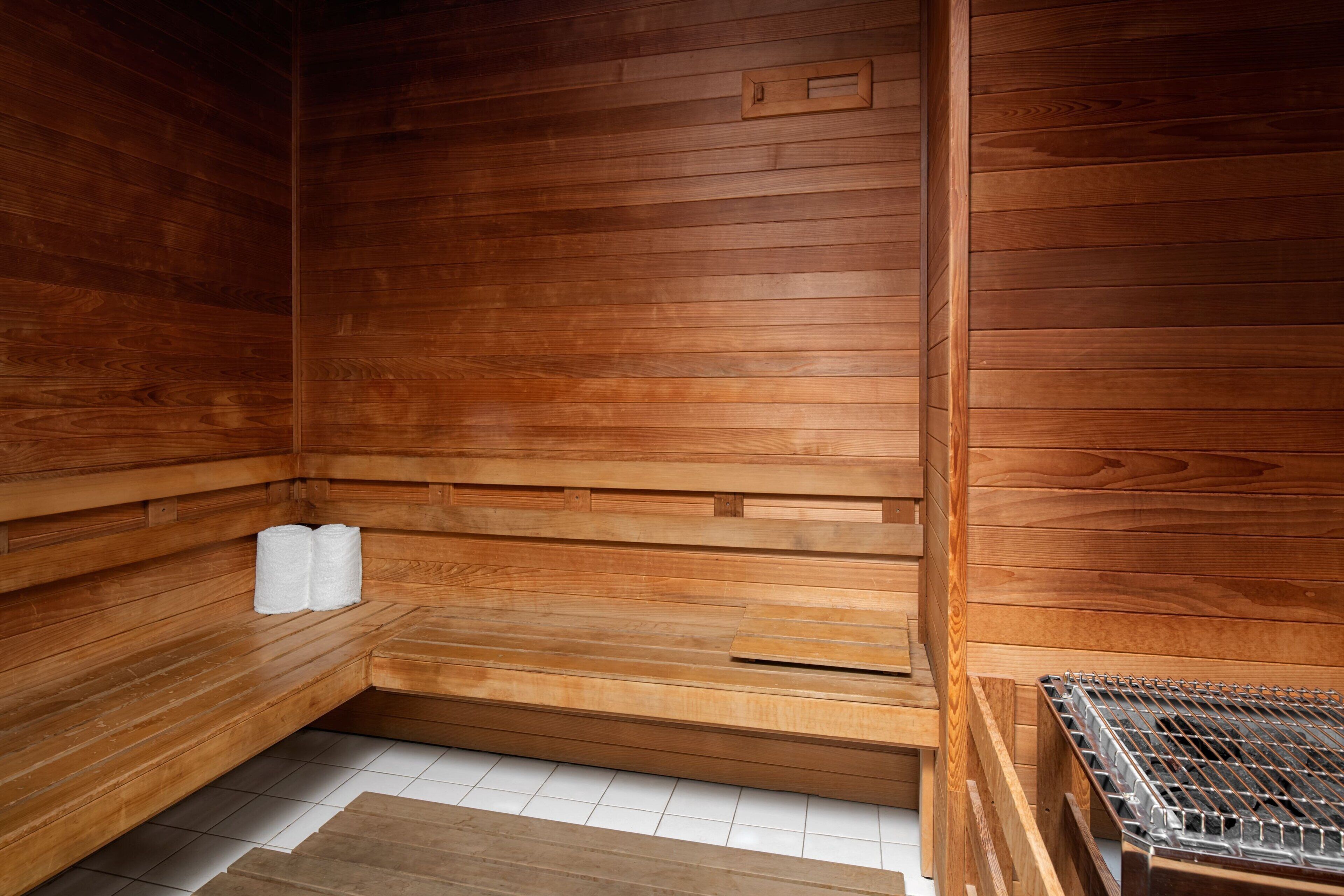 A wooden sauna with benches, a bench with towels, and a metal grate.