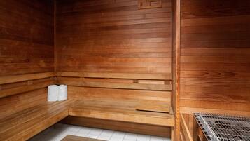 A wooden sauna with benches, a bench with towels, and a metal grate.