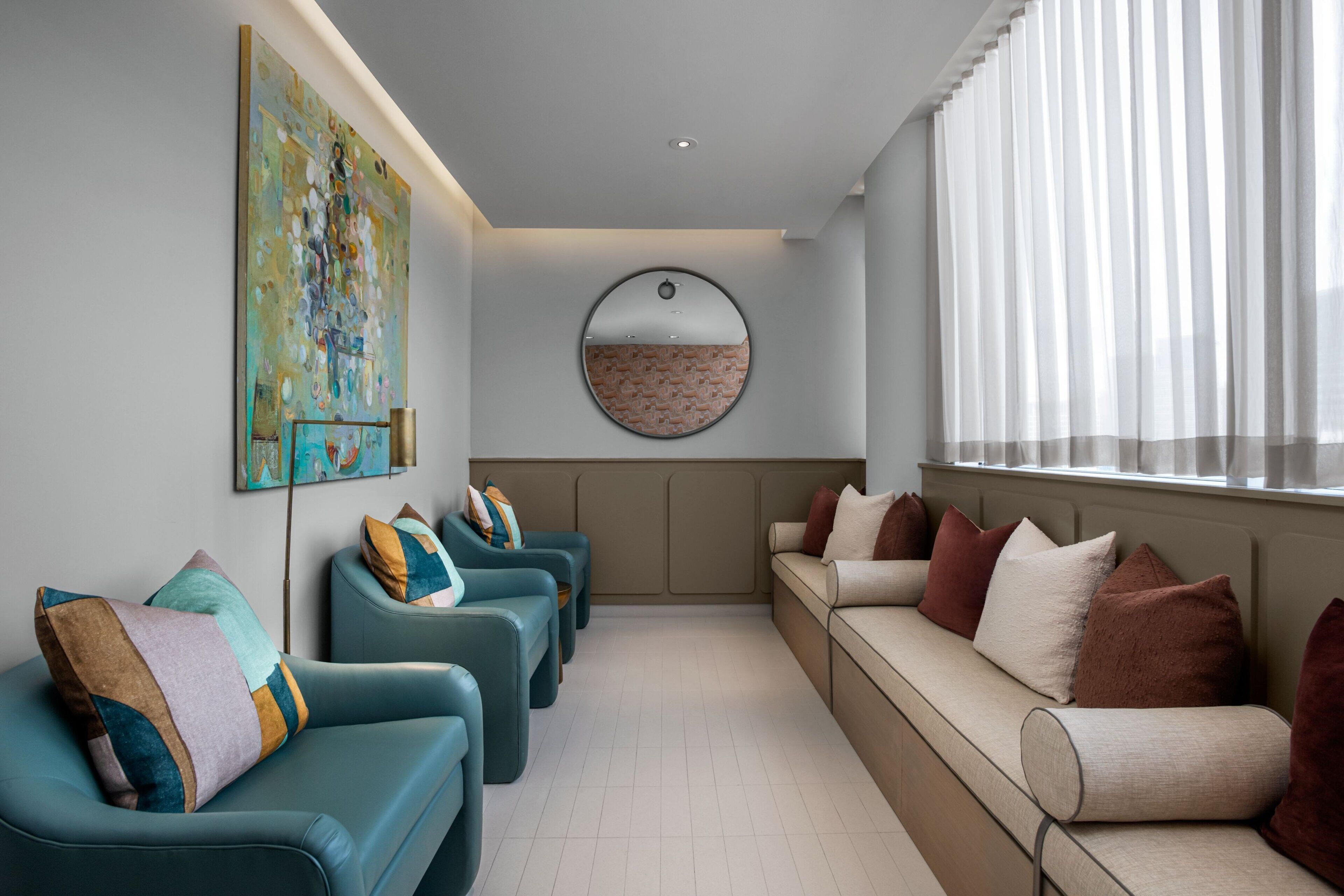 A modern lounge area with a sofa and chairs, a round mirror, and a large abstract painting on the wall.