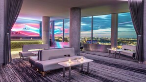 Um lounge moderno com vista para a cidade, janelas amplas e mobiliário contemporâneo.