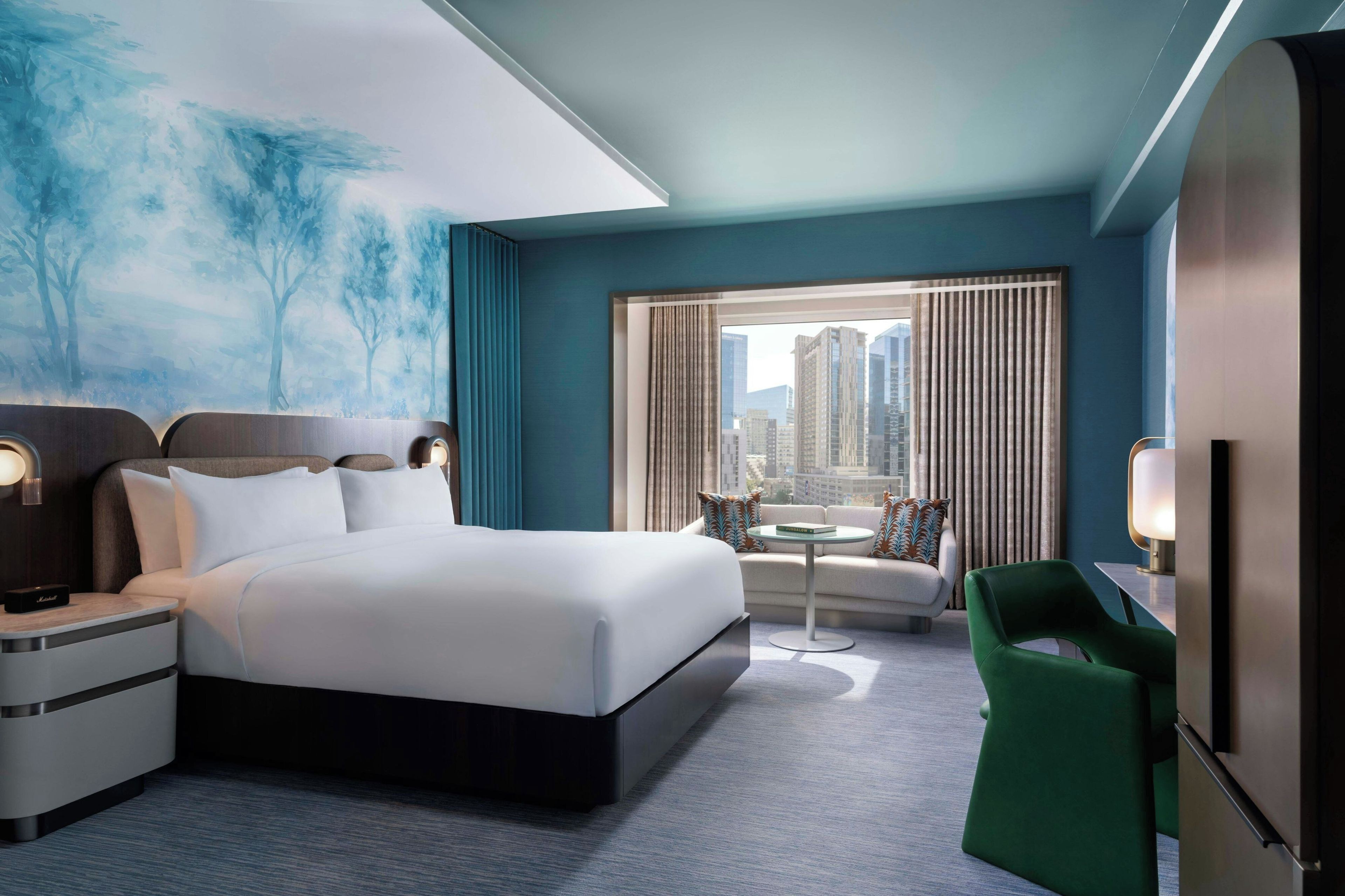 Habitación de hotel moderna con una cama grande, una zona de estar con vistas a la ciudad y un cuadro en la pared.